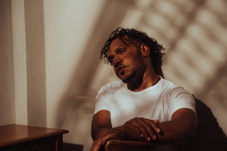 Emotional Reflection and Integration Man sitting on a chair leaning against a wall in warm lighting, reflecting on his internal journey.